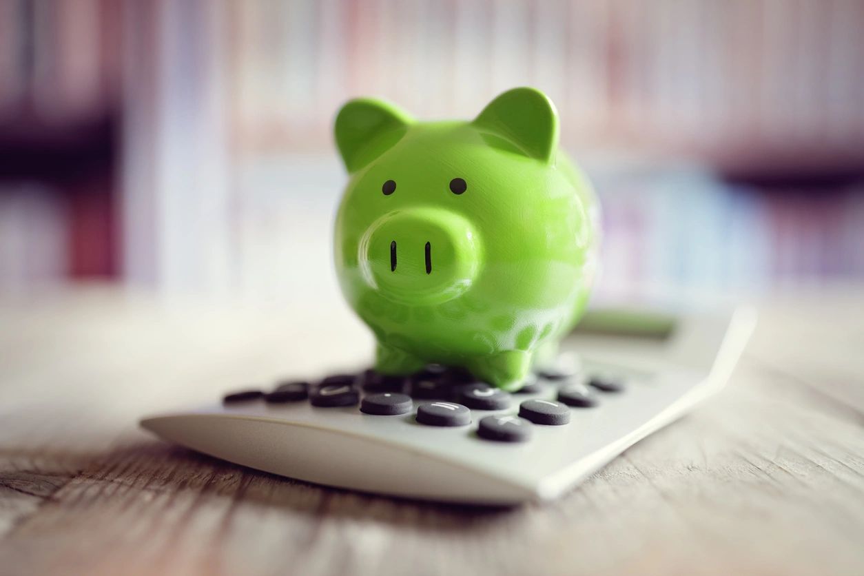 A green piggy bank sitting on top of a calculator.